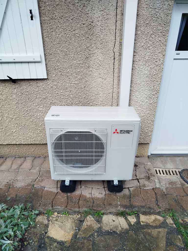 Unité extérieure Mitsubishi Electric d’un système de climatisation gainable, installée sur une terrasse en pierre contre un mur extérieur